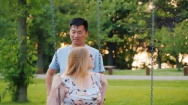 Çok ırklı çift - Asyalı adam ve hamile Kafkas kadın bir salıncak binmek. Mutlu genç aile