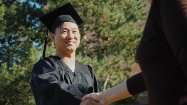 Exitoso hombre asiático en ropa de graduado acepta felicitaciones. Le dan la mano. — Vídeo de stock