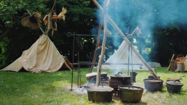 Amerikai őslakos tábor az erdőben. Étel készül az előtérben, a hagyományos wigwam sátrak láthatók mögötte. — Stock videók