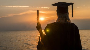 Deniz üzerinde bir günbatımı arka plan üzerinde elinde bir diploma ile bir üniversite mezunu arka görünümü. Yüksek öğretimde yeni fırsatlar