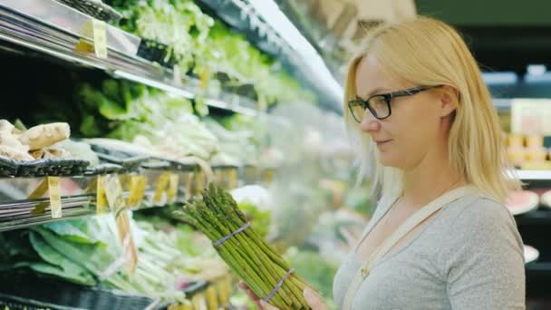 Жінка середнього віку вибирає зелену в овочевому відділенні супермаркету — стокове відео