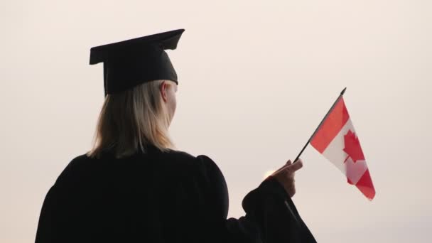 Вид сзади на выпускника с флагом Канады в руке. Обучение в Канаде — стоковое видео