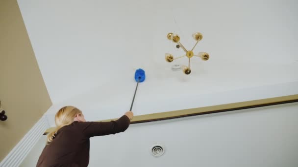Жінка чистить павутину і сміття на стелі біля люстри. Прибирання великого будинку — стокове відео