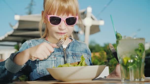 Das Mädchen isst einen köstlichen Salat auf der Sommerterrasse des Restaurants. Ruhe mit Baby-Konzept — Stockvideo
