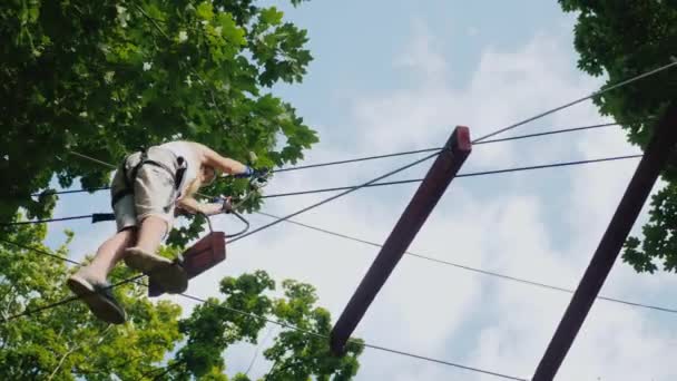 Low angle shot A brave child walks along a tightrope between tall trees. Active childhood and fun — Stock Video