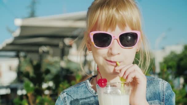 Ritratto di una ragazza divertente che beve un frullato in un bar. Riposo con bambini concetto — Video Stock