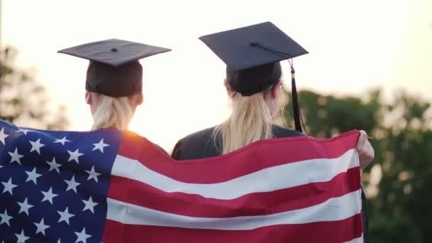 Two college graduates in gowns and caps with the American flag. Rear view