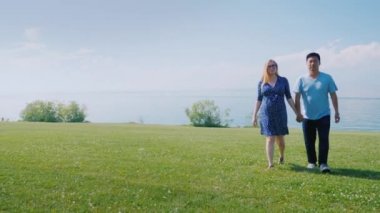 Mutlu çok ırklı çift yeşil çayırlar boyunca yürürken, ufukta güzel bulutlar olduğu ileri gitmek