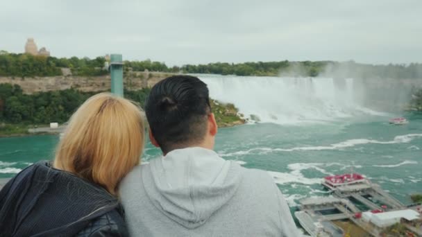 Mladý multietnický pár turistů obdivuje pohled na slavné Niagarské vodopády z kanadské strany. — Stock video