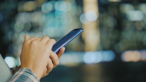 Manos de hombre con teléfono inteligente sobre fondo bokeh de las luces de la ciudad — Vídeos de Stock