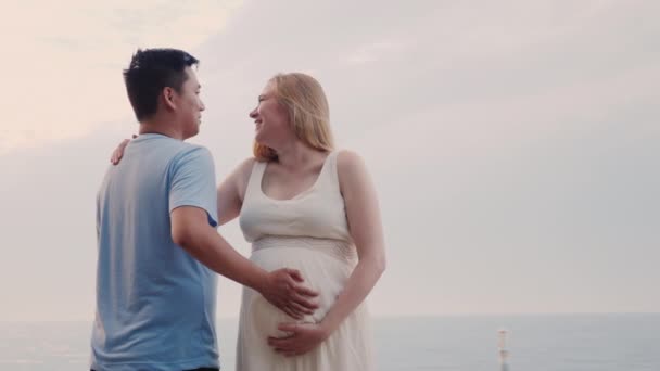 Happy young couple by the sea - Caucasian pregnant woman and her asian husband — Stock Video