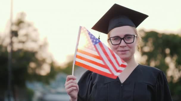 Achteraanzicht van een afgestudeerde met de vlag van de VS in de hand. Studeren in Canada — Stockvideo