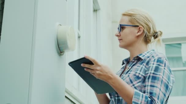 Una mujer registra las lecturas de un mostrador montado en la pared de una casa, utiliza una tableta — Vídeo de stock