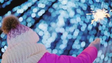 Büyük bir Noel ağacının bulanık ışıklarının arka planında Kıvılcımlı ile oynayan çocuğun arka görünümü