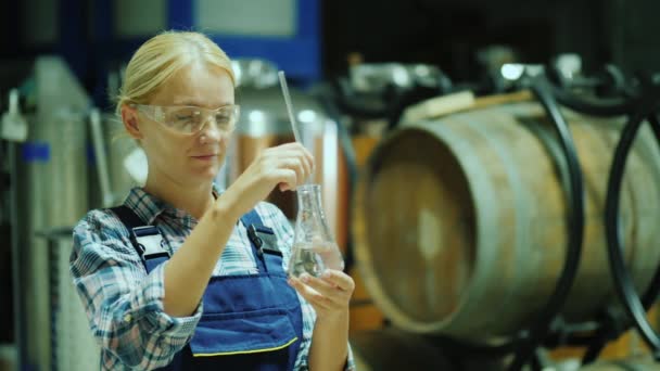 Женщина-исследователь, работающая с образцами продукции во фляжке. На фоне деревянных бочек вина — стоковое видео