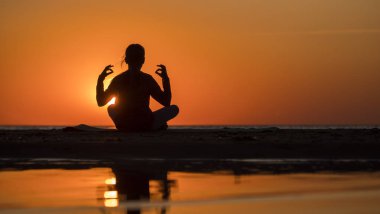 Genç kadın gün batımında nilüfer pozisyonunda denizin yanında oturur, meditasyon yapar