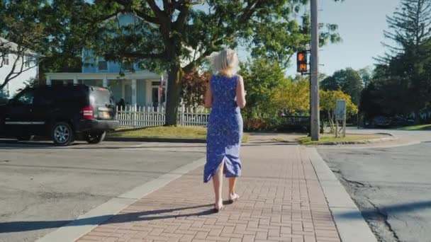 A mulher cruza a estrada em um pedestre que cruza ao sinal permissivo de um semáforo. Uma pequena cidade típica americana — Vídeo de Stock