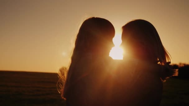 Een vrouw met een dochter in haar armen. Zacht naar elkaar kijken, silhouetten bij zonsondergang — Stockvideo