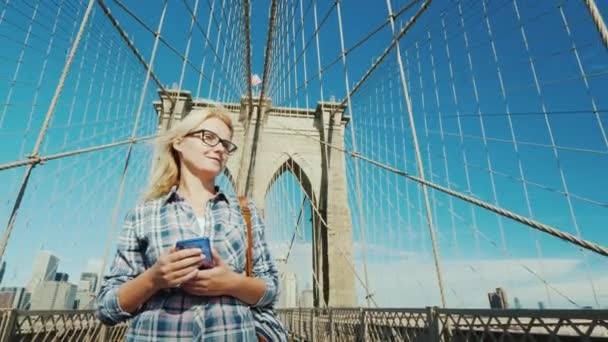 Молода жінка з телефоном в руці, йдучи по Бруклінському мосту в Нью-Йорку — стокове відео