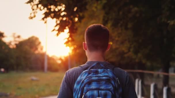 Um adolescente com uma mochila nas costas anda pelo beco — Vídeo de Stock