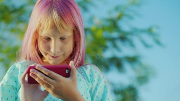 Uma menina com cabelo rosa está usando um smartphone rosa . — Vídeo de Stock