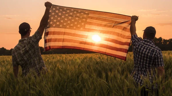 Zwei Männer hissten energisch die US-Flagge in einem malerischen Weizenfeld — Stockfoto