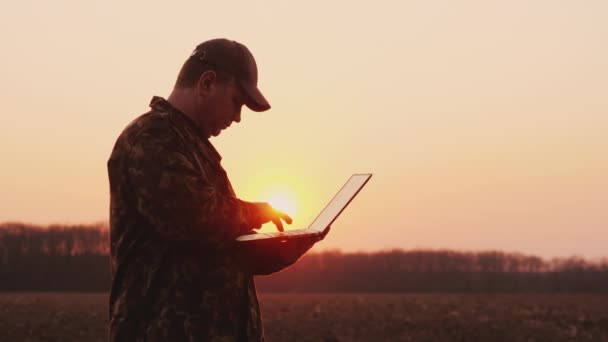 Granjero serio trabajando con el ordenador portátil en el campo al atardecer. Planificación de la siembra — Vídeo de stock