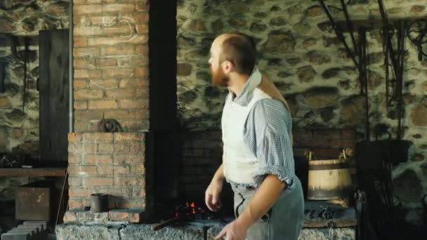 Genesee, NY, USA, July 2019: A blacksmith in antique clothing from the time of the development of America forges an iron product in a forge — Stock Video