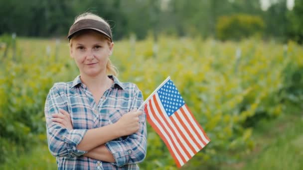 カメラを見て、アメリカの旗を持つ女性農家。アメリカの農家の肖像 — ストック動画