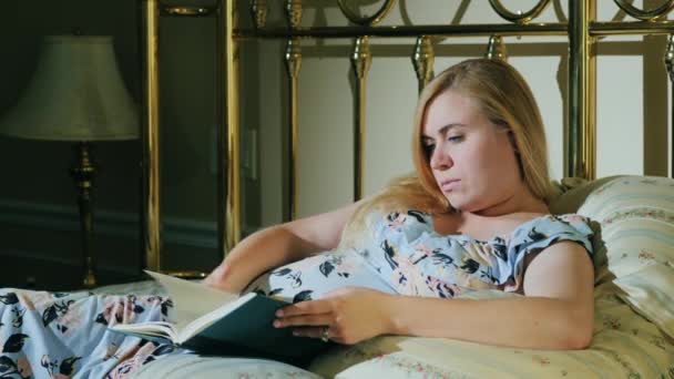 Беременная женщина читает книгу в постели — стоковое видео
