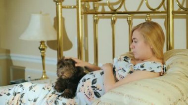 Onu okşayan hamile bir kadının karnında bir köpek yavrusu yatıyor.