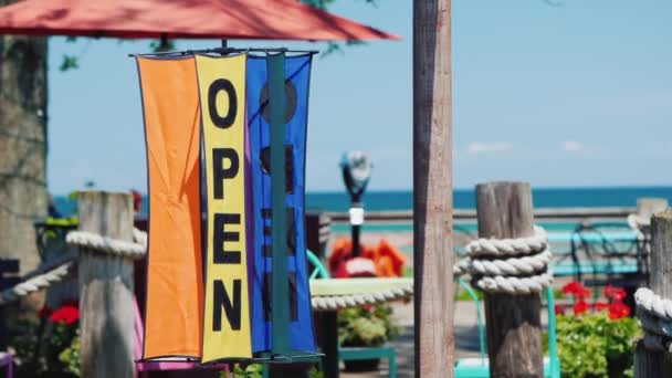 Inscriptie open op een roterende weer wijzer. Tegen de achtergrond van de zee en de zomer cafés. Reisseizoen concept — Stockvideo