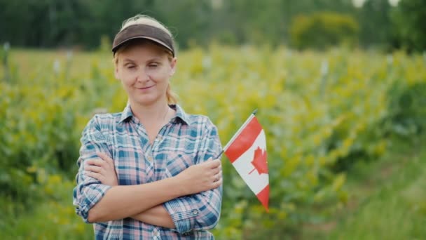 カメラを見てカナダの旗を持つ女性農家。カナダの農家の肖像 — ストック動画
