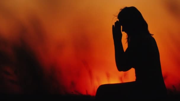 Женщина средних лет молится на закате, высокая трава качается на переднем плане — стоковое видео