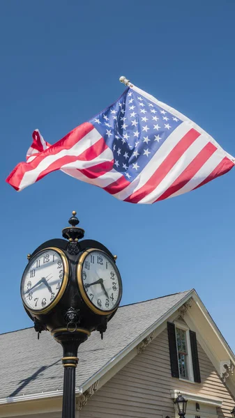 Antike Uhr auf einer Säule, ein Holzhaus im Hintergrund und die US-Flagge - amerikanisches Outback-Konzept — Stockfoto