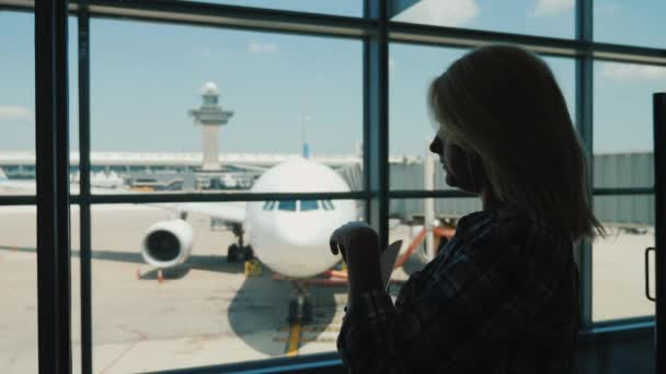 Силуэт женщины у окна терминала аэропорта, поедающей закуски во время ожидания рейса — стоковое видео