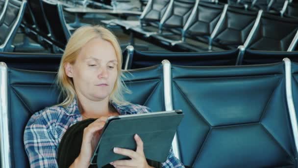 Una mujer usa una tableta en un salón del aeropuerto. Ocio vuelo pendiente — Vídeos de Stock