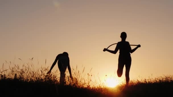 Тренування на свіжому повітрі - силует жінки, що стрибає через мотузку на заході сонця — стокове відео