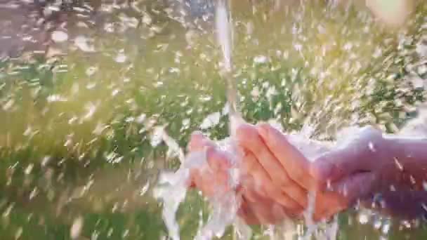 El agua fluye en palmas humanas abiertas. Salpicaduras efectivamente volar aparte en el sol — Vídeos de Stock