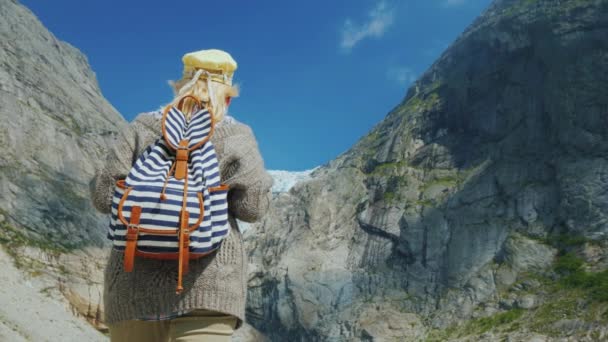 A woman in warm clothes admires the glacier high in the mountains. Briksdal glacier in Norway, a trip to the northern countries of Europe — Stock Video