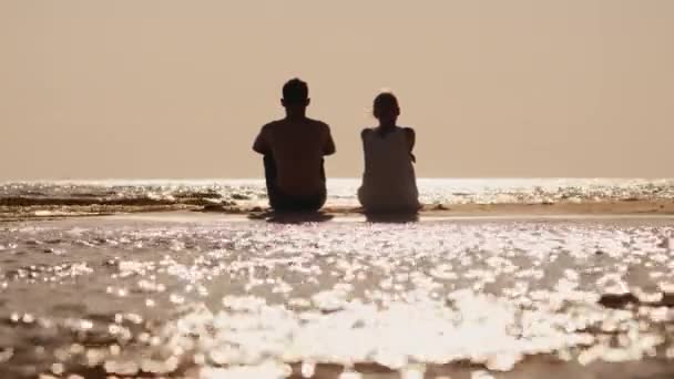 Um jovem casal se senta em uma ilha de areia e olha para a frente para o horizonte — Vídeo de Stock