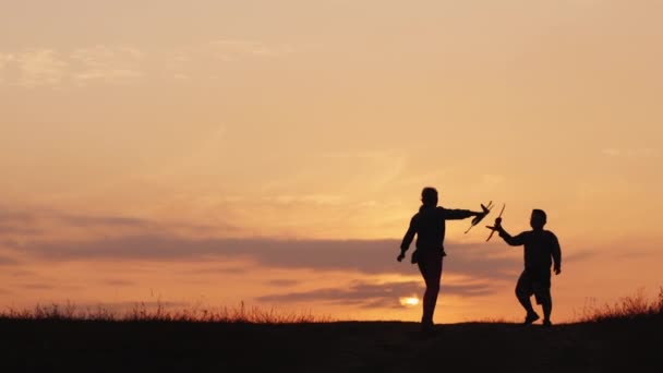 Silhouetten eines Mädchens und eines Jungen, die bei Sonnenuntergang mit Flugzeugen spielen. Eine glückliche und unbeschwerte Kindheit — Stockvideo