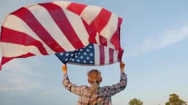 アメリカ国旗を手に走り、空を背景に手を振って旗を振り、後ろの景色 — ストック動画