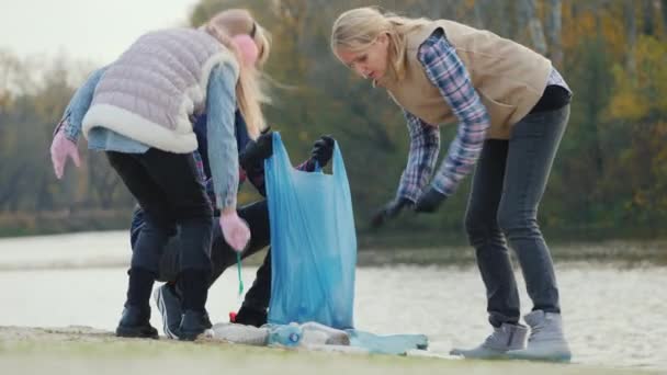 Uma mulher com filhos apanha lixo no lago. Voluntários coletam resíduos plásticos — Vídeo de Stock