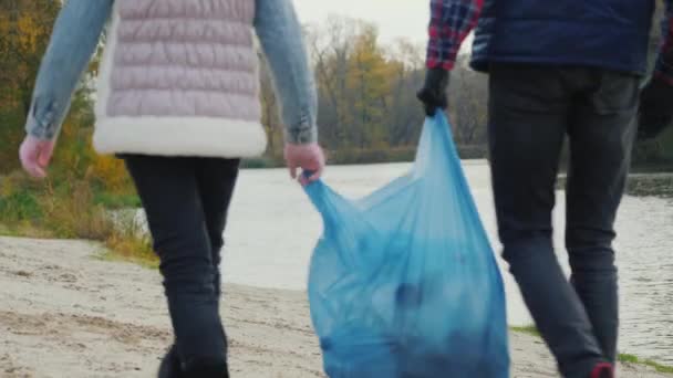 Діти-добровольці несуть мішок сміття, ходять уздовж берега озера, де збирають сміття — стокове відео