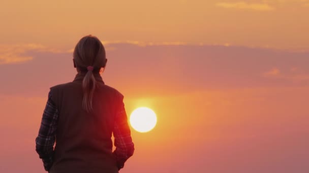 Silhouet van een vrouw van middelbare leeftijd die naar de ondergaande rode zon gaat — Stockvideo
