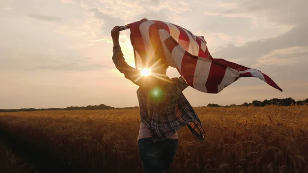 Žena s vlajkou USA běhá na slunci na pšeničném poli — Stock fotografie