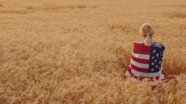 Omzunda Usa bayrağı olan bir kadın buğday tarlasında duruyor.