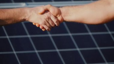 Güneş panellerinin arka planında iki adamın el sıkışması