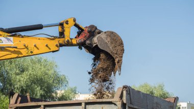 Kazı kovası kamyona toprak döküyor.